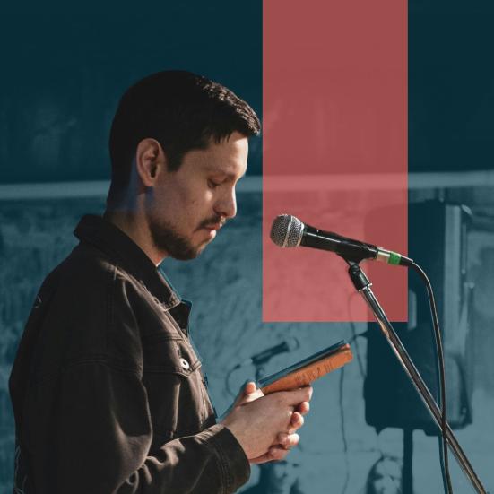 Mand læser op ved mikrofon og står med bog i hånden